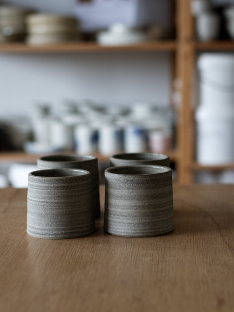 Kopjes handgemaakt van donkere klei met ongeglazuurde buitenkant in een setje van 4 stuks op een houten tafel