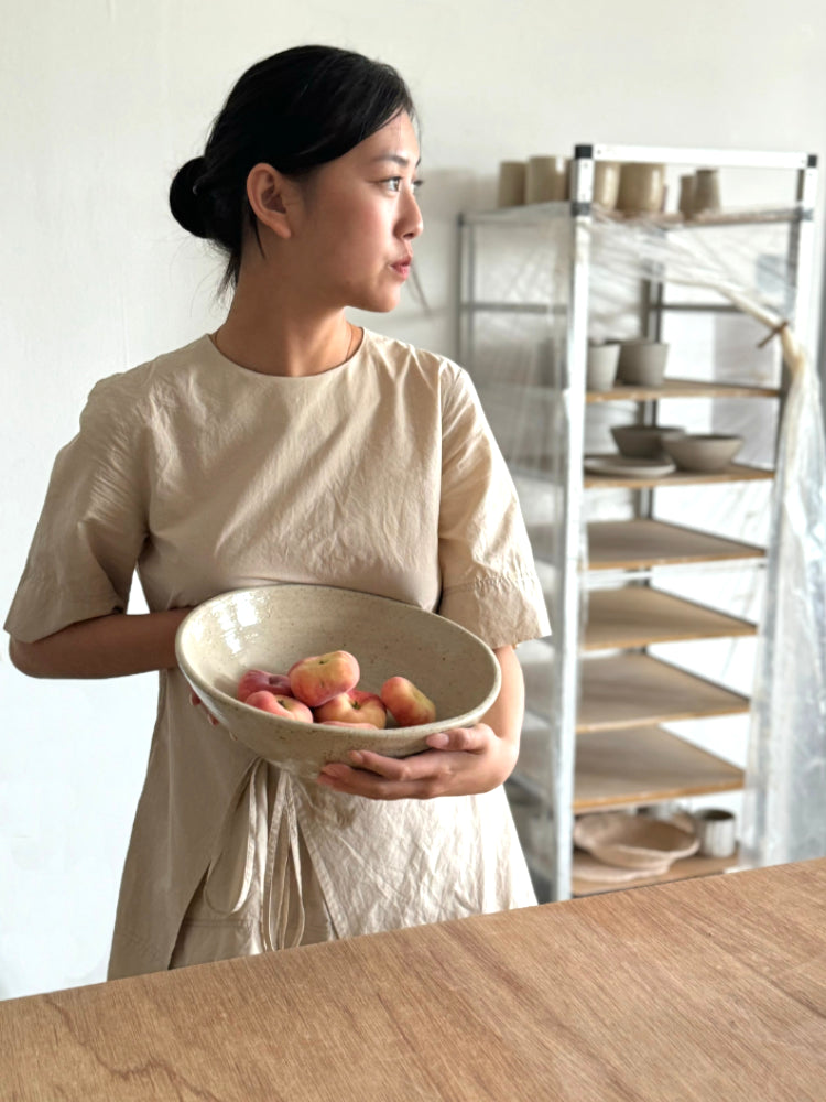 meisje die een grote keramieken schaal perziken vasthoudt op een atelier met een hele slowliving vibe