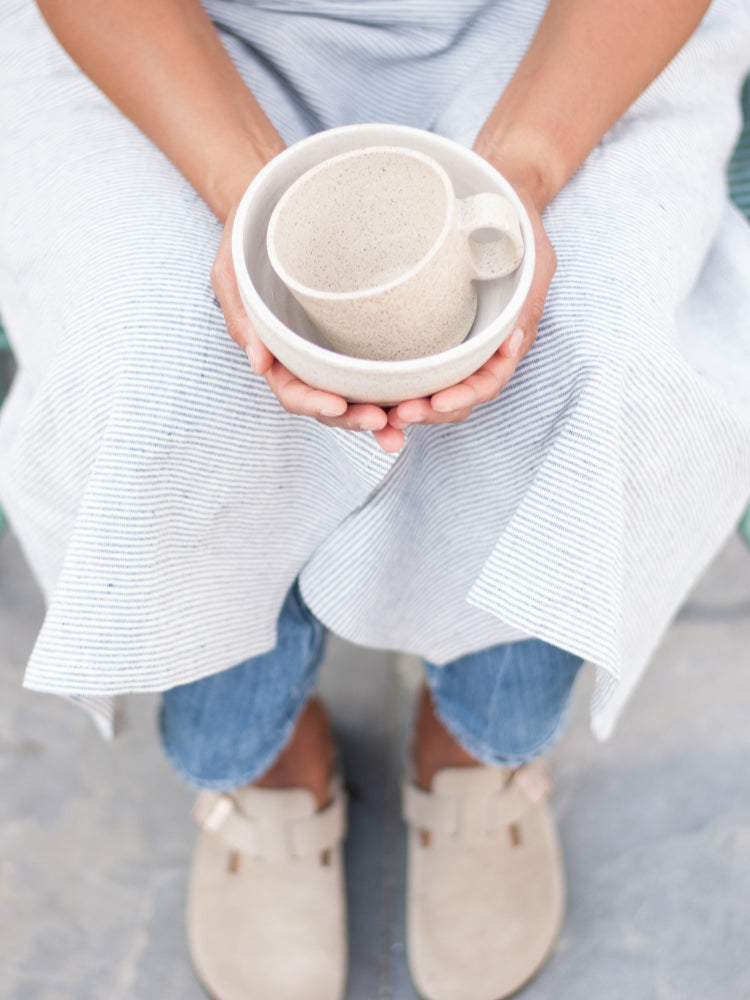 Lichtgespikkelde handgemaakte mok en kom in een schoot van iemand die een schort draagt