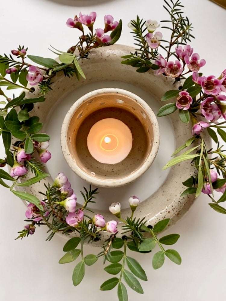 Bovenaanzicht van de ronde handgemaakte bloemenvaas met roze bloemen, en een brandend theelichtje in het midden