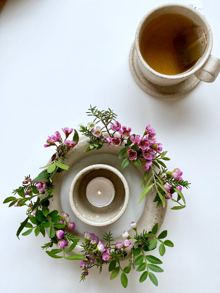 Ronde handgemaakte bloemenvaas met roze bloemen, een theelichtje in het midden en mok, bovenaanzicht
