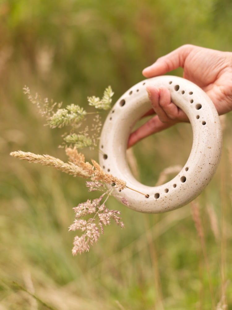 Ronde bloemenvaas vastgehouden door een hand met gras vaag  in de achtergrond 