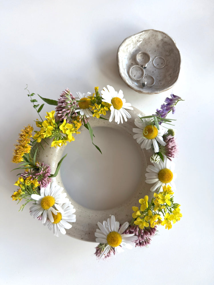 Handgemaakte ronde bloemenvaas met verschillende gekleurde bloemen en een schaaltje met ringen ernaast