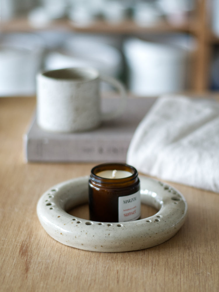 Handgemaakte ronde beige vaas en natuurlijke geurkaars op houten tafel