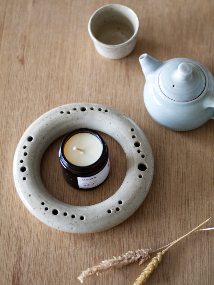 Ronde vaas met een geurkaars in het midden naast een theepotje en kopje
