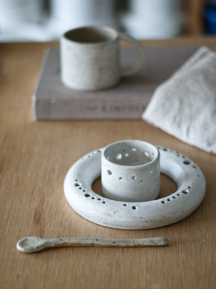 Ronde handgemaakte vaas met theelichtje in whitewashed glazuur, naast een boek en keramische lepel