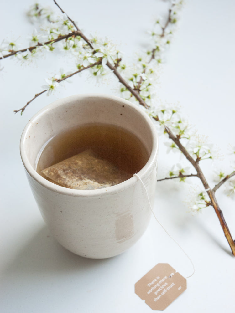 Handgemaakte theekop met een theezakje erin en een bloesemtak ernaast