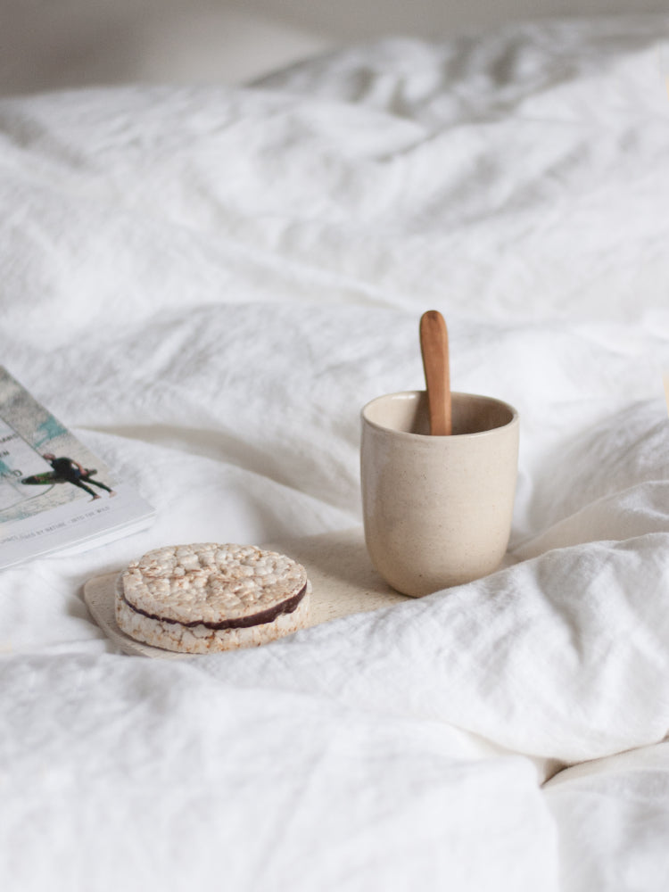 Handgemaakte theekop op een dienblad in bed tussen zachte dekens met magazine ernaast