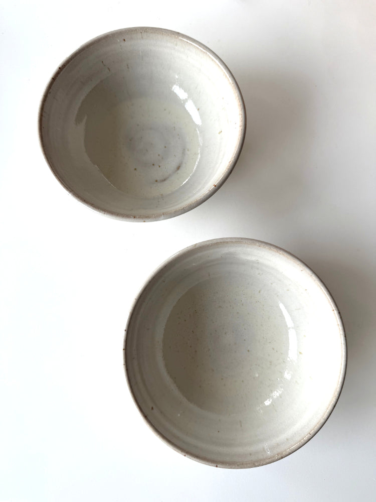 twee handgemaakte kommen met wit glazuur op een witte tafel