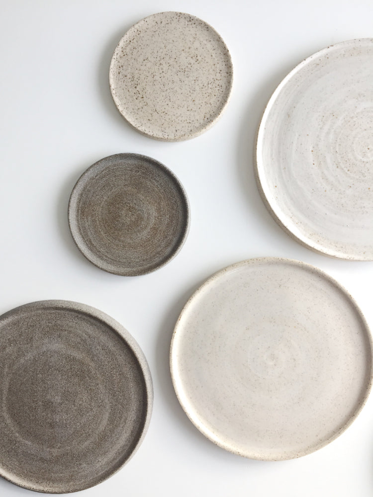 Verschillende handgemaakte cakeborden en schotels, bruine en wit gespikkelde, bij elkaar gefotografeerd op een witte achtergrond