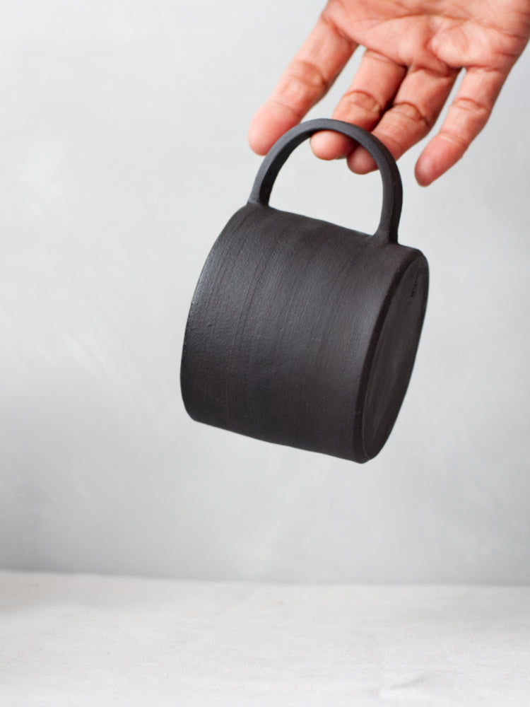 Hand die een handgemaakte zwarte mok aan het oortje vasthoudt