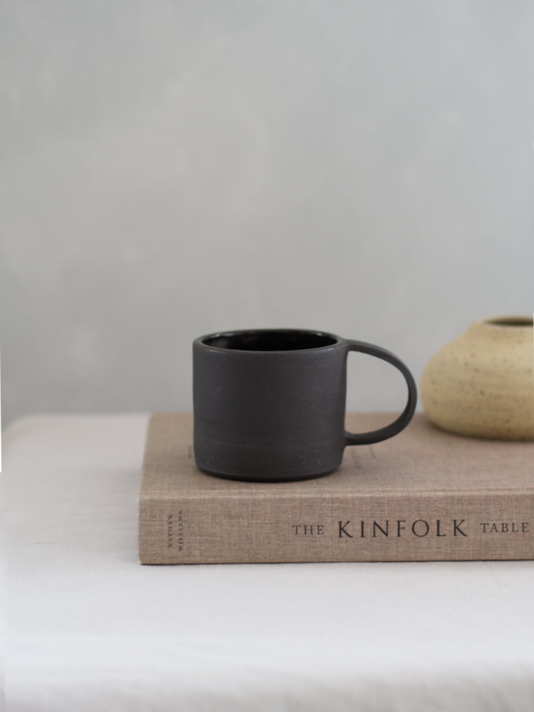 Handgemaakte zwarte keramieken mok op een Kinfolk boek in slow living stijl